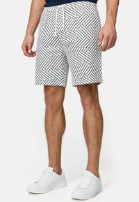 Pantalones cortos de hombre con estampado, hechos de un tejido ligero. Presentan una base blanca con un patrón geométrico en zigzag negro. Cintura elástica con cordón de ajuste.
