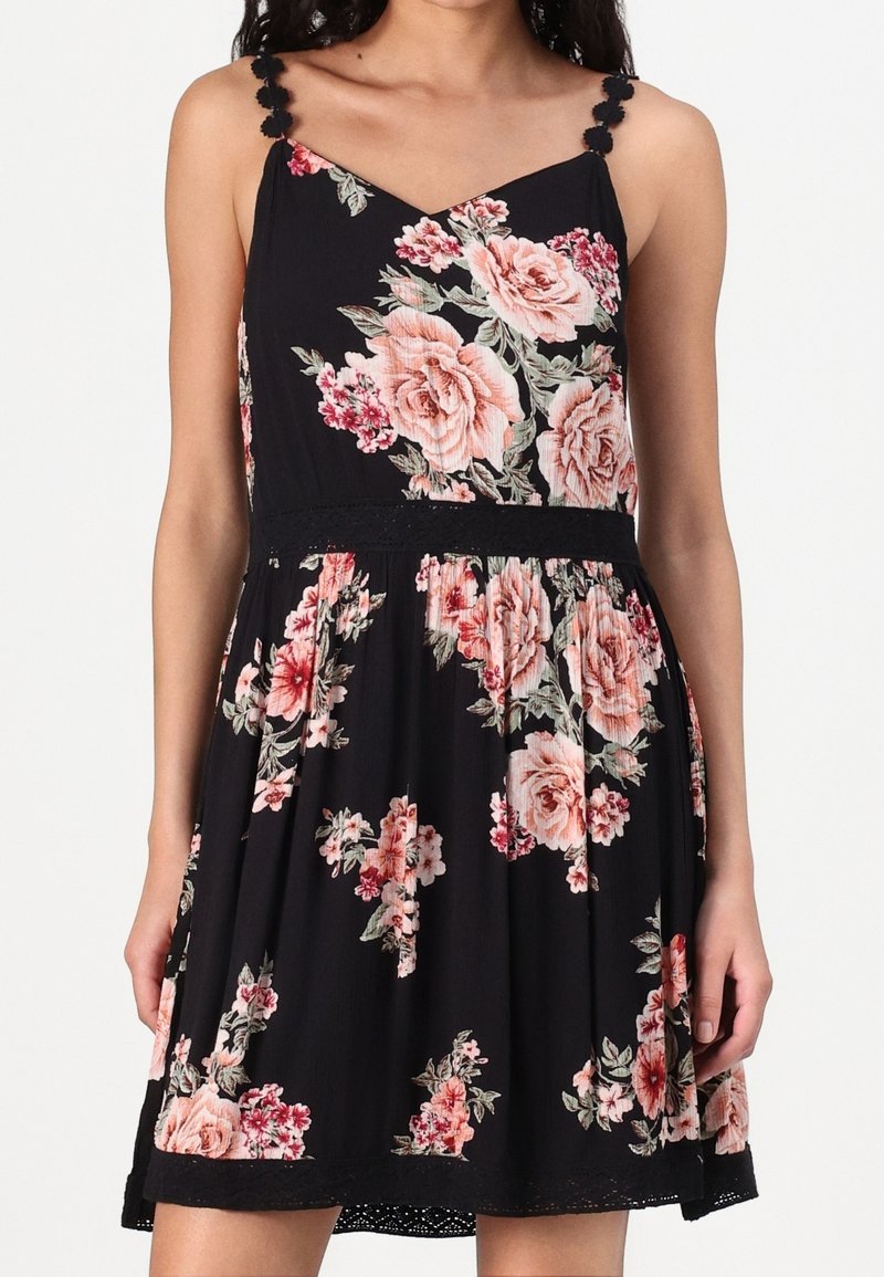 Robe noire sans manches avec motifs floraux roses et rouges, bretelles décoratives et taille cintrée.