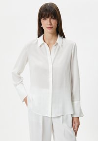 Witte zijden blouse met een knoopsluiting aan de voorkant, lange mouwen en een ontspannen pasvorm. Kenmerkt een klassieke kraag en een licht afgeronde zoom.
