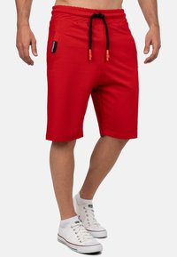 Rode shorts gemaakt van zachte stof met een elastische tailleband, verstelbaar trekkoord en zijzakken. Ontworpen met een relaxte pasvorm en omgeslagen zoom.