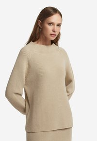 Beige, gerippter Strickpullover mit Rundhalsausschnitt und lockerer Passform. Verfügt über lange Ärmel und einen geraden Saum, was ein strukturiertes Erscheinungsbild verleiht.
