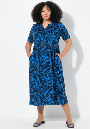 Maxikleid mit blauem und schwarzem Blumenmuster, kurzen Ärmeln, V-Ausschnitt, geraffter Taille und Seitentaschen. Getragen mit blauen Absatzsandalen.