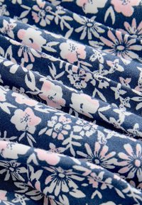 Tessuto blu con motivi floreali bianchi e rosa chiaro, mostrato piegato con texture e dettagli di tessitura visibili.