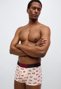 Μπεζ ανδρικά μπόξερ με σχέδια κόκκινων κερασιών, με μαύρη ελαστική μέση με την επωνυμία «DIESEL» σε κόκκινο χρώμα. Μαλακό, ελαστικό ύφασμα.