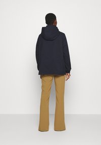 Námořnická kapucňová bunda s volným střihem, dlouhými rukávy a dohotovenými švy, v kombinaci se žlutými rozšířenými kalhotami. Hladká textura, ležérní design.