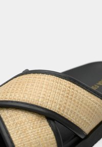 Sandale à glissière noire avec un matériau naturel tissé sur la partie supérieure. Fini texturé et semelle noire élégante offrant un contraste.