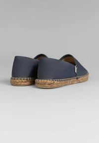 Zapatillas de lona azul marino sin cordones con suela de yute trenzado, parte trasera redondeada y una pequeña etiqueta de logo en el lateral. Textura suave y diseño minimalista.