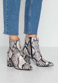 Snake print ankle boots in black and white, featuring a high block heel and a side zip closure. Textured finish adds dimension.