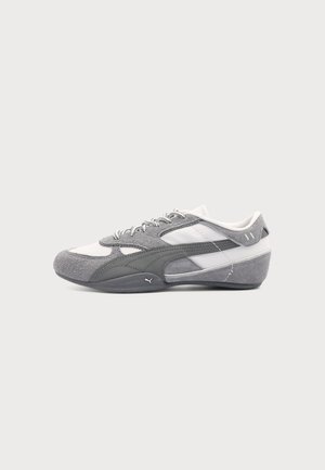 Grå og hvid lavprofileret Puma-sneaker med ruskind- og mesh-detaljer, snørebånd og en buet sål mod en ensartet lys baggrund.