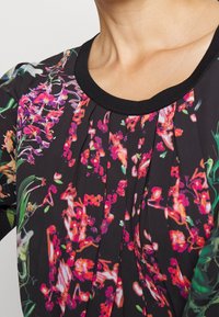 Blumenbluse aus schwarzem Stoff mit lebhaften pinken und orangefarbenen Blumenmustern, Rundhalsausschnitt und plissierten Details an der Vorderseite.