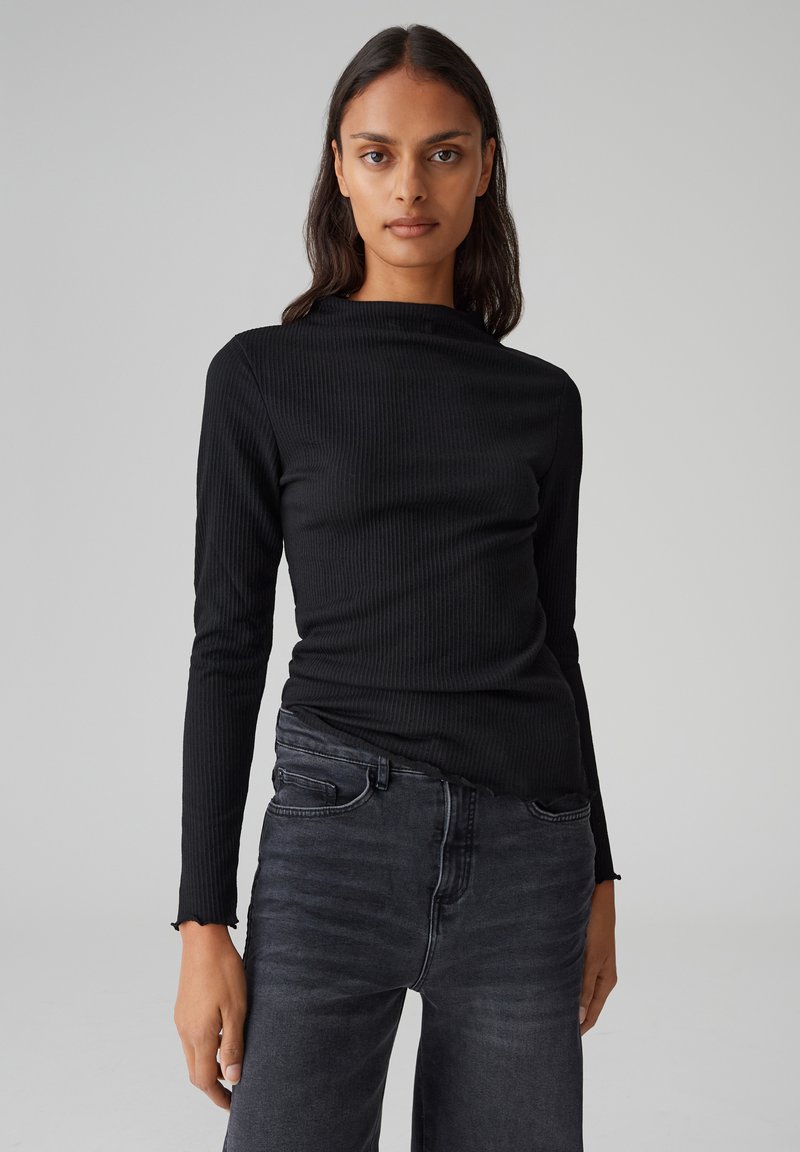 Schwarzes, geripptes Langarmoberteil mit rundem Ausschnitt, kombiniert mit dunkelgrauen Jeans, die eine subtile Textur und eine lockere Passform haben.