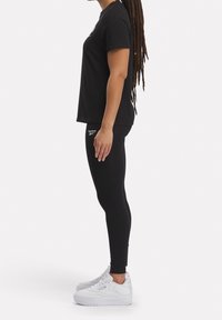 Camiseta negra de manga corta y leggings negros ajustados, completados con zapatillas deportivas blancas con suela gruesa y acentos del logotipo.