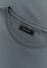 Camiseta de algodón gris con cuello redondo y una etiqueta negra con "Matinique". El material es suave con una textura sutil.