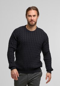 Maglione girocollo in blu navy scuro a trecce, con polsini e orlo a coste. La texture presenta un motivo a incrocio.