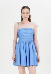 Light blue dress with a fitted bodice featuring horizontal pleats, thin adjustable straps, and a flared skirt. Smooth cotton fabric.