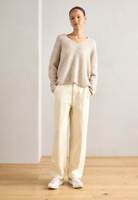 Maglione beige a maglia con scollatura a V, abbinato a pantaloni a gamba larga color crema e sneakers bianche, creando una palette neutra e delicata.