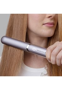 Piastra per capelli Remington, superficie metallica argentata, design arrotondato, con un pulsante di accensione e logo, tenuta vicino a lunghi capelli lisci e setosi.