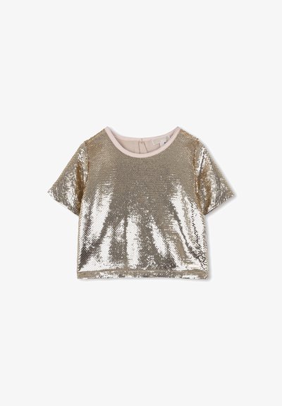 Īsām piedurknēm zelta sekvīnu ievērojams topluks ar apaļu izgriezumu un bēša apdari uz baltā fona.