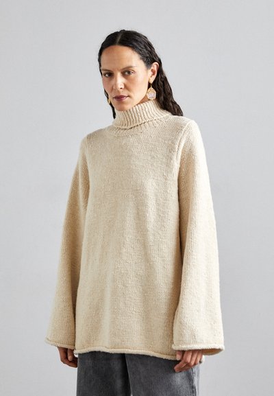 Pull en maille beige à col roulé avec des manches surdimensionnées et une finition texturée. Il présente un col côtelé et un design à coupe décontractée.