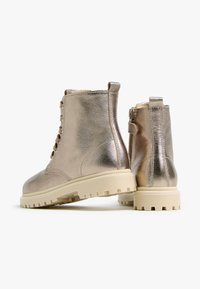 Metallisch goldene Knöchelstiefel mit Schnürsenkeln, strukturiertem Finish und Gummisohle. Mit einem Reißverschluss an der Seite und einem robusten Profildesign.