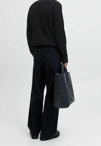 Pull noir côtelé assorti à un pantalon noir à jambes larges. La personne tient un sac fourre-tout noir texturé avec de courtes poignées.