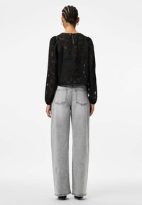 Juoda nėrinėlių palaidinė su pūstomis rankovėmis, su raktelio formos iškirpte nugaroje. Derinama su laisvais šviesiai pilkos spalvos džinsais.