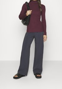 Bourgogne-ribbad polotröja i kombination med vida marinblå byxor. Svart axelväska med texturerad rem och platta svarta sandaler.