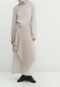 Lyserød strikket sweater med høj kædehals, parret med et matchende indpakningsskørt med asymmetrisk kant og sidelukning.