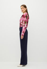 Färgglad blus i rosa, grön och vit mönster med långa ärmar, i kombination med marinblå byxor och vita spetsiga klackskor.