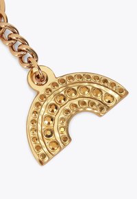 Złoty charms w kształcie półksiężyca z łańcuszkiem. Posiada okrągłe nity i gładkie wykończenie, odbijając światło drobną fakturą.