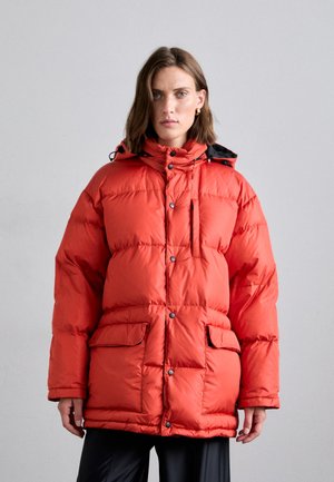 Oranje pufferjack met een capuchon, met grote doorgestikte secties, drukknopen en twee voorzakken. Gemaakt van een gladde, glanzende stof.