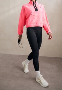 Vaatteet ovat vaaleanpunainen neljännesvetoketjupulli, jossa on mustia yksityiskohtia ja suuri etutasku; yhdistetty mustiin leggingsseihin, joissa on teksturoitu kuvio, ja valkoisiin tennareihin.