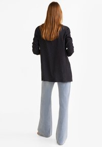 Schwarzes Langarmshirt mit weißen Pünktchen, lockerer Schnitt, mit einem Rückenschlitz, kombiniert mit hellblauen Schlagjeans.