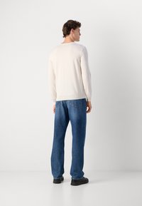 Maglione a maniche lunghe beige chiaro con scollatura rotonda, abbinato a jeans denim blu larghi e calzature nere. Design minimalista, texture liscia.