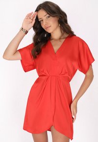 Rochie scurtă roșie din satin, cu decolteu în V, mâneci scurte și talie plisată. Fusta are un tiv rotunjit.