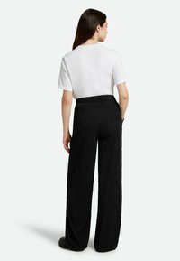 Black pleated wide-leg pants with a textured fabric, paired with a white short-sleeve t-shirt. Features an elastic waistband and side pockets.
