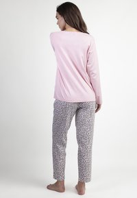 Top de manga larga rosa combinado con pantalones de pijama de estampado de leopardo. Tejido suave, corte recto y detalles mínimos en un ajuste relajado.