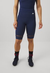 Marineblauwe sportshorts van rekbaar materiaal met meshpanelen op de dijen. Gepaard met zwarte sokken en donkere sneakers.