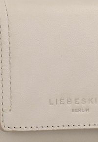 Cartera de cuero crema con textura suave, que presenta el nombre de la marca embosado "LIEBESKIND BERLIN" y una fina costura a lo largo de los bordes.