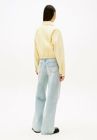 Geel cropped jack met een gladde textuur, voorzien van een kraag en knoopmanchetten, gecombineerd met lichtblauwe flared denim jeans.