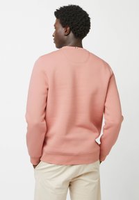 Felpa rosa realizzata in morbido tessuto, con scollatura rotonda, maniche lunghe e polsini a costine, abbinata a pantaloni di colore chiaro.