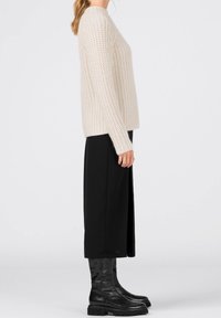 Chunky stickad krämfärgad tröja med långa ärmar, matchad med svart flödande kjol och höga, glänsande svarta stövlar med tjock sula.