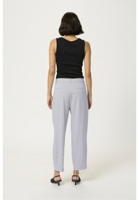 Czarny top bez rękawów, jasnoszare dopasowane spodnie z tylnymi kieszeniami i czarne buty na obcasie, widok z tyłu na jasnym tle.