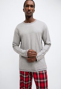 Pelēka garām piedurknēm krekls ar apaļu kakla izgriezumu un redzamām šuvju detaļām, kombinēts ar sarkaniem un melniem pledētu raksta pidžamas biksēm.