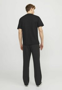 Camiseta de algodón negra con mangas cortas y cuello redondo; combinada con pantalones negros. Diseño sencillo y de corte relajado sin logotipos visibles.