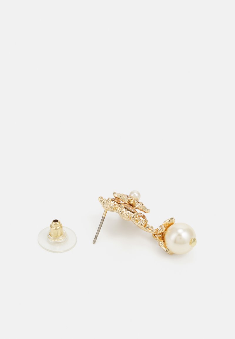Boucles d'oreilles en métal doré ornées d'un design décoratif avec un accent en perle, un clou en métal et un support en caoutchouc translucide.
