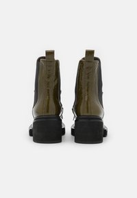 Glossy olive green ankle boots with black elastic side panels and chunky black heels, viewed from the back on a white background.
