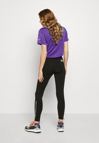 Leggings noirs avec le logo "The North Face" en blanc, associés à un t-shirt violet à manches courtes. Les chaussures présentent des accents gris, violet et rouge.