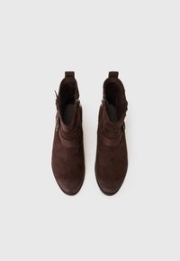 Bottines en daim marron avec des semelles noires, dotées de zips sur les côtés et d'une sangle décorative sur le devant. Texture lisse et design à bout rond.