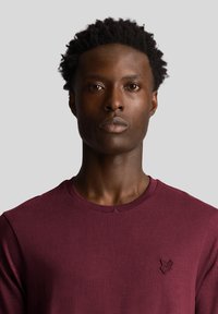 Camicia bordeaux a maniche lunghe realizzata in tessuto texturizzato, con scollatura rotonda e un piccolo logo ricamato sul petto.